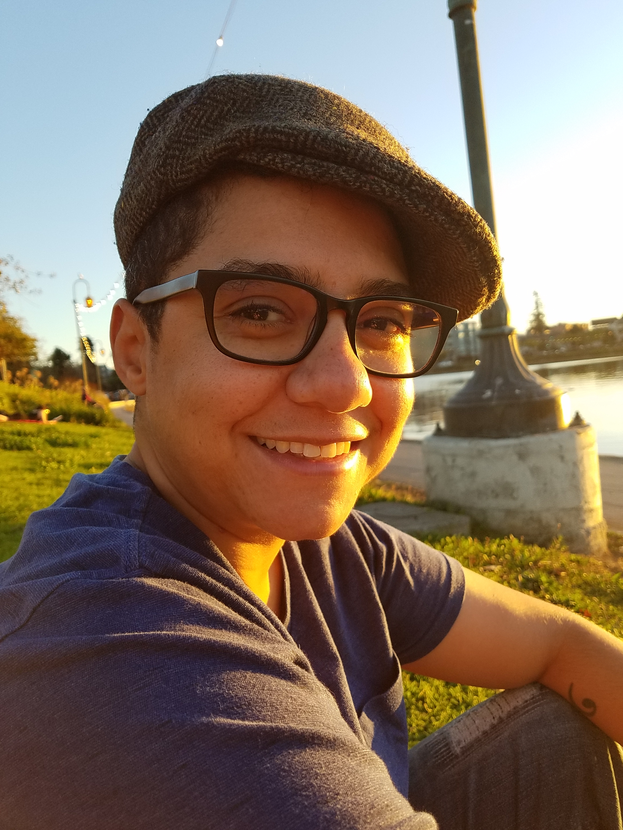 Jack smiles at the camera, wearing a cap and glasses, seated next to Lake Merritt in Oakland